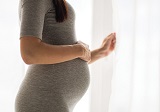 A pregnant woman standing by the curtains with her hand on her stomach