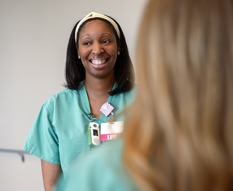 Closeup of a young female labor and delivery LPN smiling during a morning huddle in the hospital hallway.