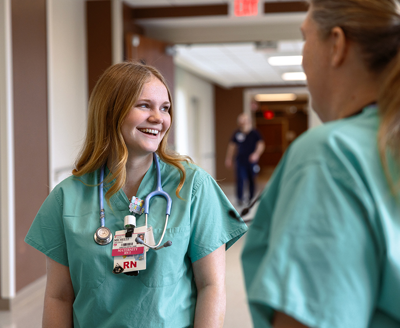 A smiling blonde maternity RN participates in a team meeting with another charge nurse to ensure consistent patient care. 